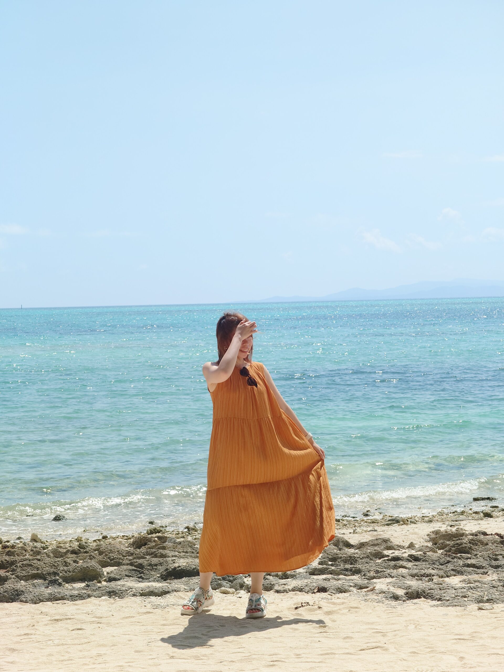 青い海を背景にオレンジ色のワンピースで過ごす今崎光美さん